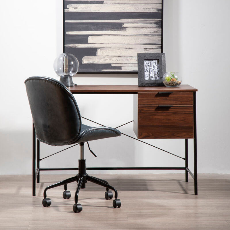 Modern office desk with black chair, framed artwork, and decorative items against a white wall.
