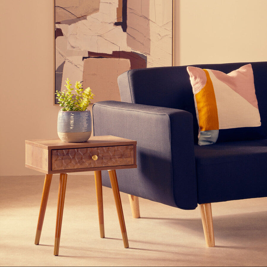 Navy blue sofa with a colorful pillow in a room with a side table and abstract wall art.
