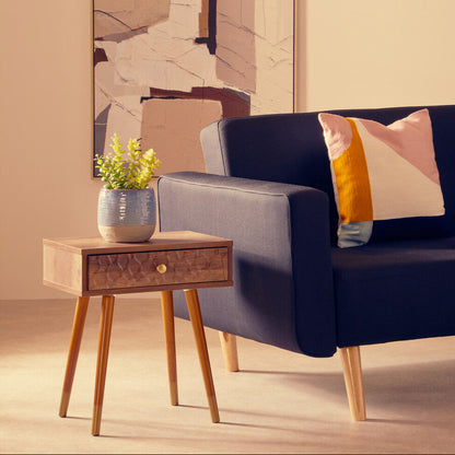 Navy blue sofa with a colorful pillow in a room with a side table and abstract wall art.