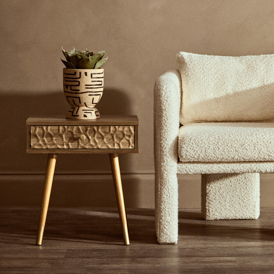 Wooden side table with a textured surface and a plant next to a textured beige sofa.