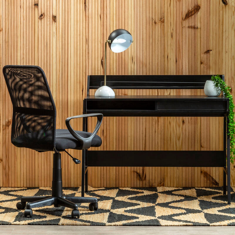 Black office chair and desk against a wooden wall with a geometric rug.