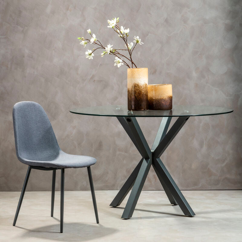 Modern glass dining table with metal legs and a gray chair against a gray wall.