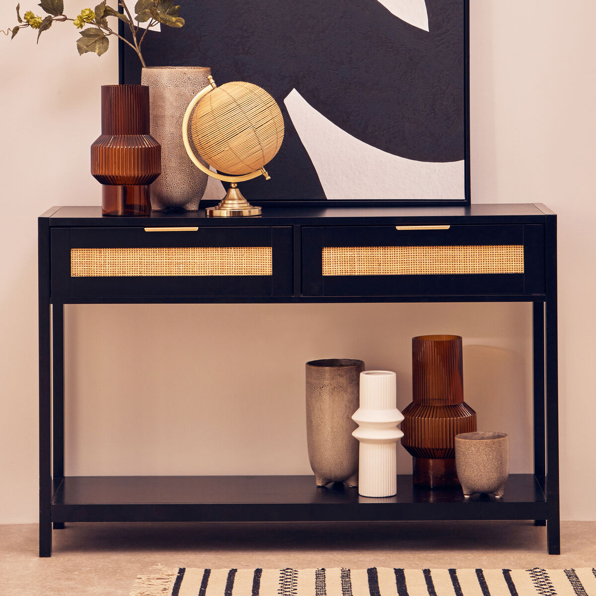 Console table with decorative items including vases and a globe against a wall with abstract art.