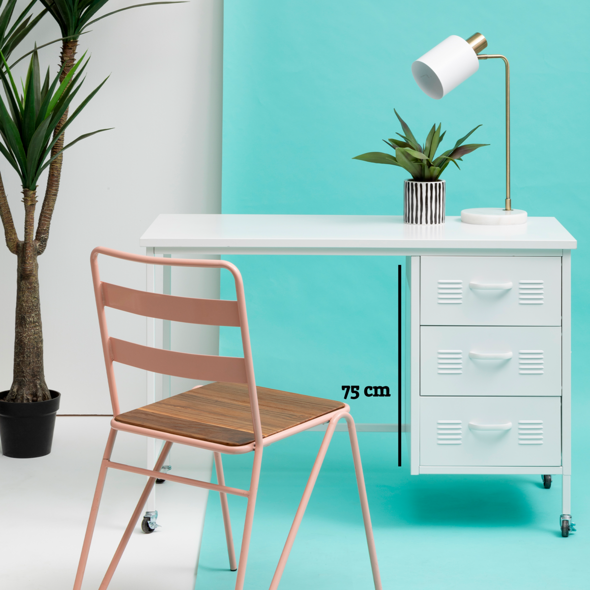 Modern desk with white surface, lamp, and plant against a turquoise wall with a pink chair.
