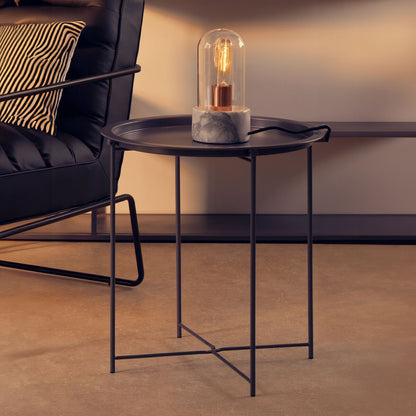 Small black metal table with a decorative lamp in a living room setting.