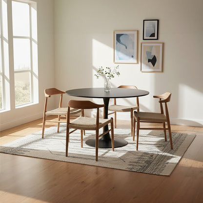 Dining room with a round black table and wooden chairs, light-colored walls, and large windows.