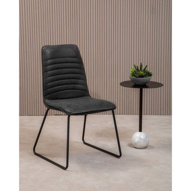 Black upholstered chair with a small round table and plant against a striped wall.