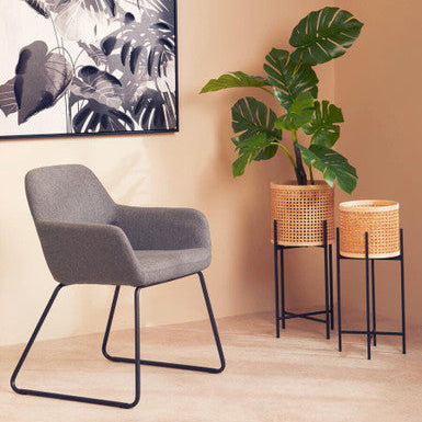 Gray chair in a room with two potted plants and a leafy artwork on the wall.