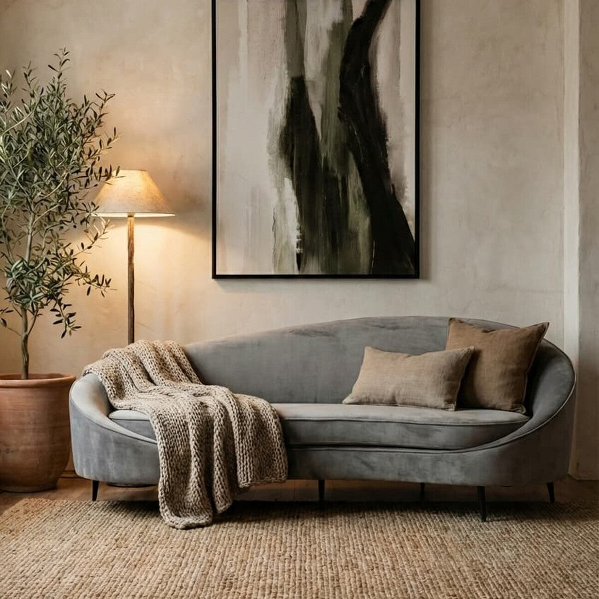 Gray sofa with pillows and a blanket in a living room setting with abstract art and a plant.