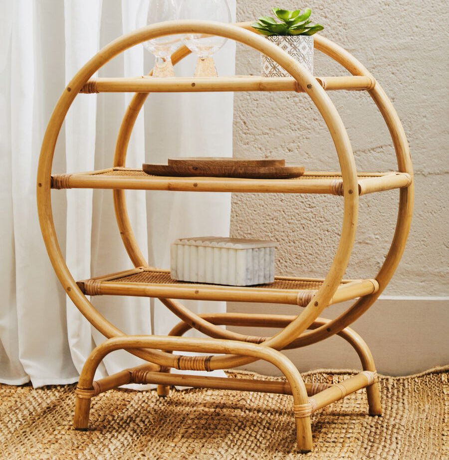 Round bamboo shelf with decorative items against a neutral wall.