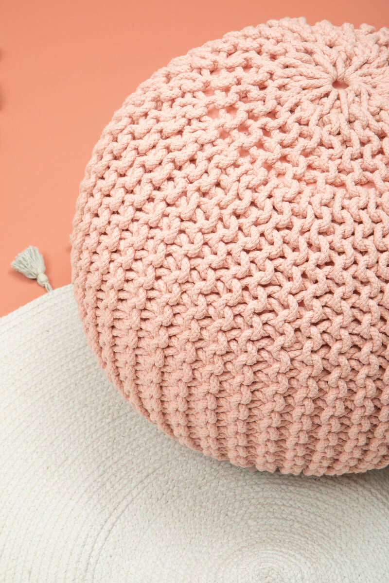 Pink knitted pouf on a light green surface with a pink background