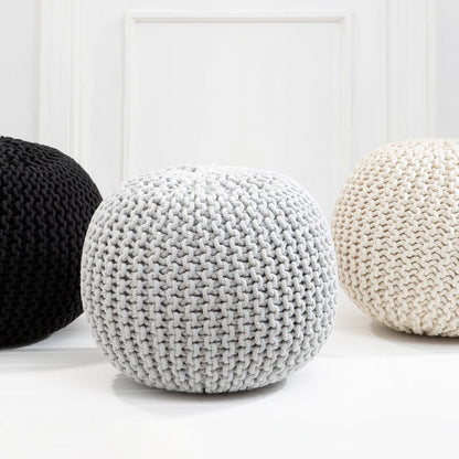 Three knitted poufs in black, white, and gray on a light wooden floor.