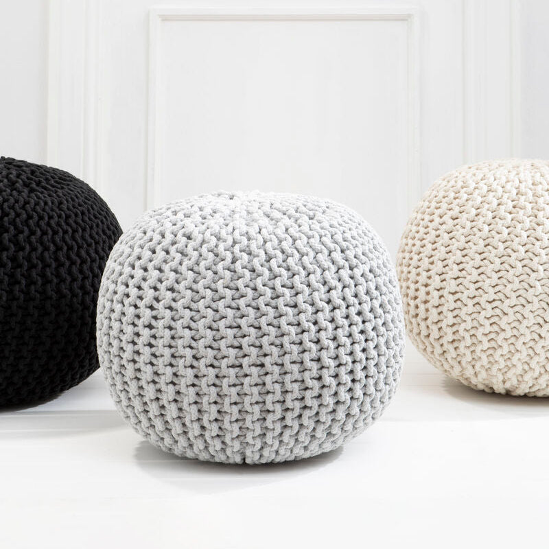 Three knitted poufs in black, white, and gray on a light wooden floor.