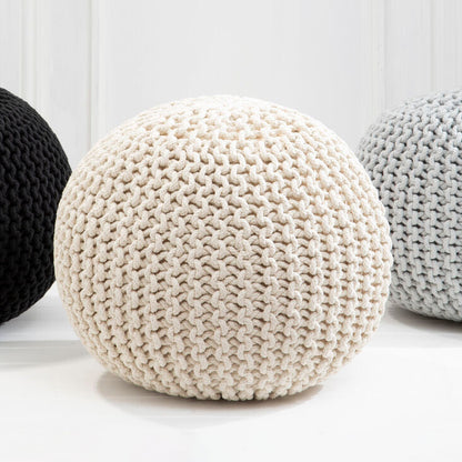 Three knitted poufs in black, white, and gray on a light wooden floor.