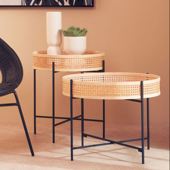 Wicker chair and ottoman with a side table against a beige wall with a leafy plant artwork.
