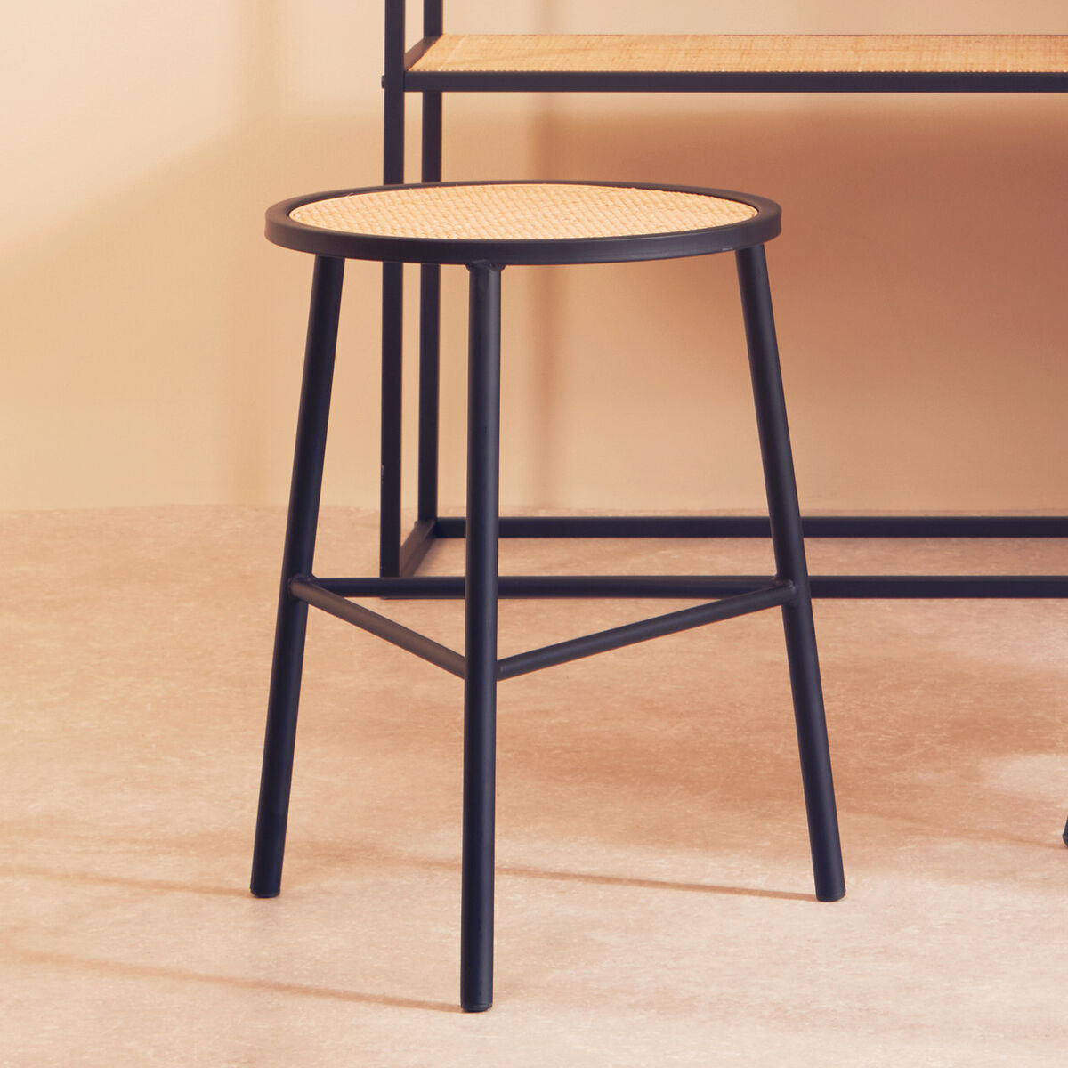 Black metal stool with woven seat on a wooden floor