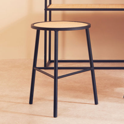 Black metal stool with woven seat on a wooden floor