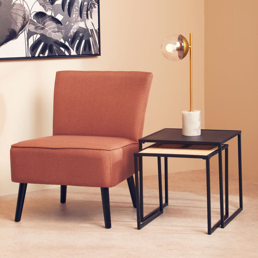 Brown chair and small black table against a beige wall with a decorative plant painting.