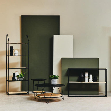 Modern interior with black shelving units, a round coffee table, and decorative items against a neutral wall.