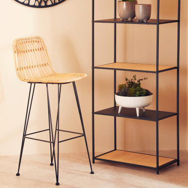 Black metal shelving unit with wooden shelves, a wicker bar stool, and decorative wall art.