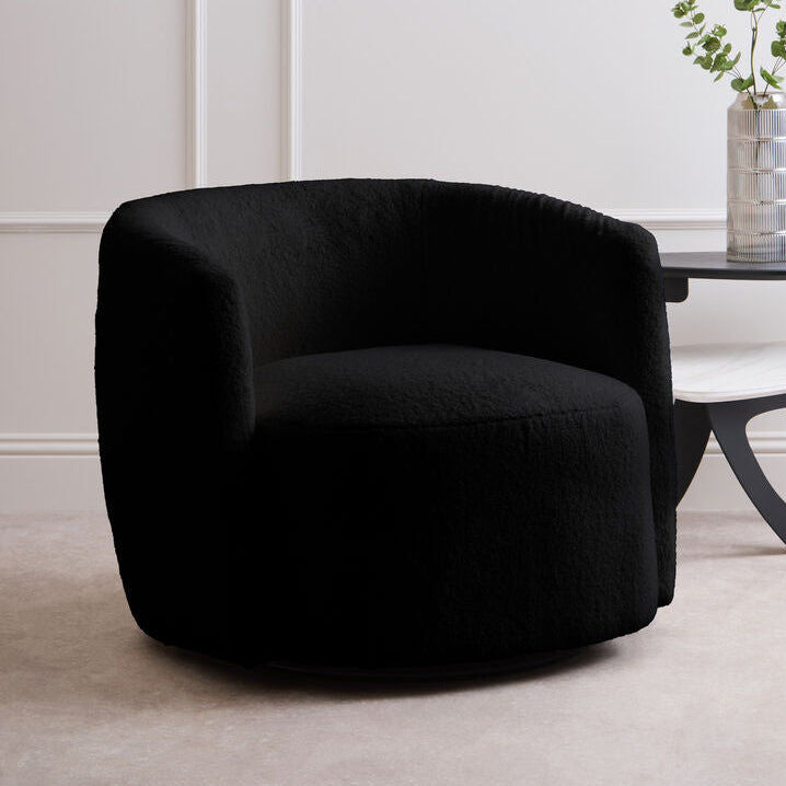 Black armchair in a minimalistic room with a white wall and a small table with a plant.