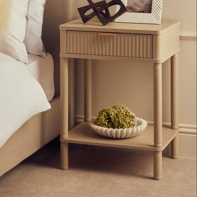 Beige nightstand with decorative items next to a bed in a bedroom setting