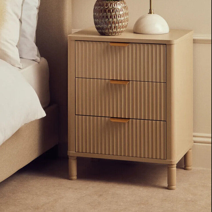 Beige nightstand with decorative items next to a bed in a bedroom setting
