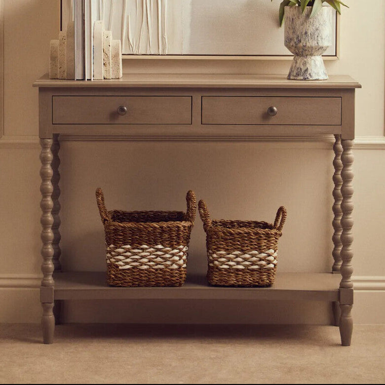 Wooden console table with two drawers and a shelf, featuring wicker baskets and decorative items.