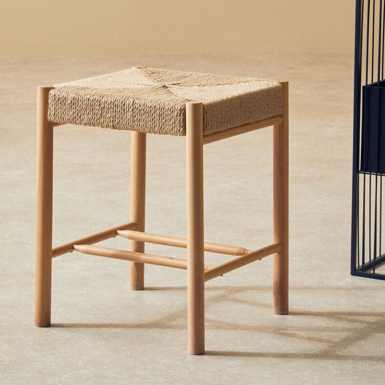 Wooden stool with woven seat next to a black metal plant stand on a beige floor.