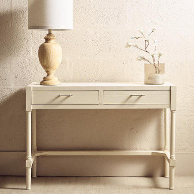 Light-colored console table with a lamp and decorative vase against a neutral wall.