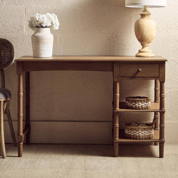 Wooden desk with lamp, vase, and chair against a textured wall.