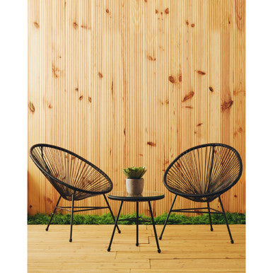 Two black wicker chairs with a small round table on a wooden deck against a wooden wall.