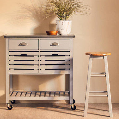 Kitchen island cart with drawers, a plant, and a stool against a beige wall.