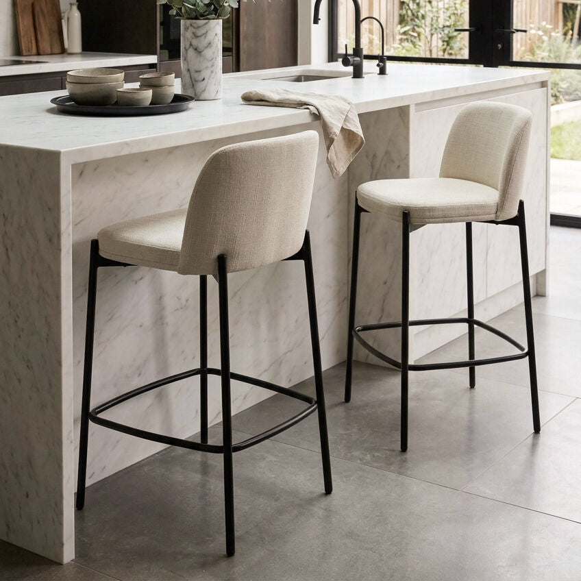 Two bar stools in a modern kitchen setting with marble island and black fixtures.