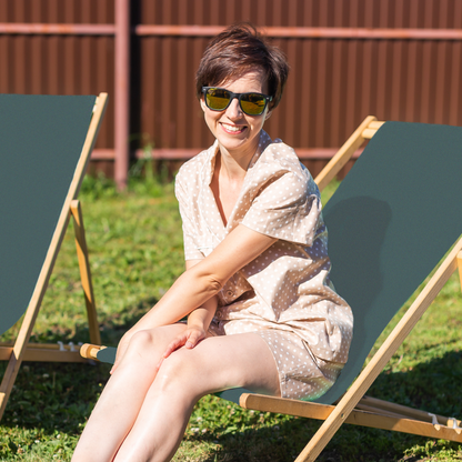 Woman sitting on a green deck chair in a garden wearing sunglasses.