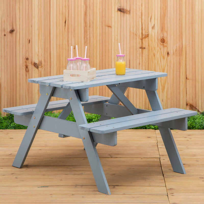 Gray picnic table with drinks on a wooden deck against a wooden fence.