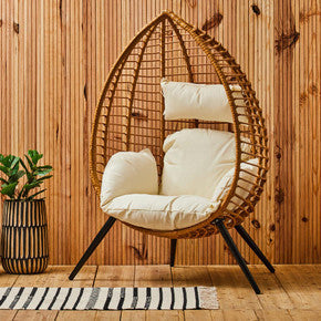 Wicker egg-shaped chair with white cushions in a room with wooden walls and floor.