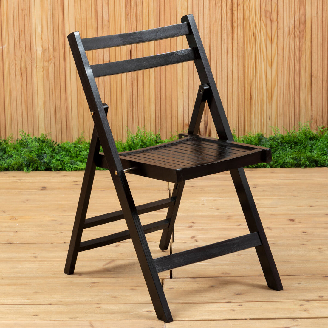 Black folding chair on a wooden deck with a wooden wall and greenery in the background