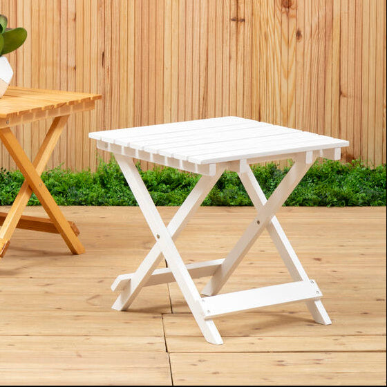 Two folding tables, one wooden and one white, on a wooden deck with a wooden fence background.
