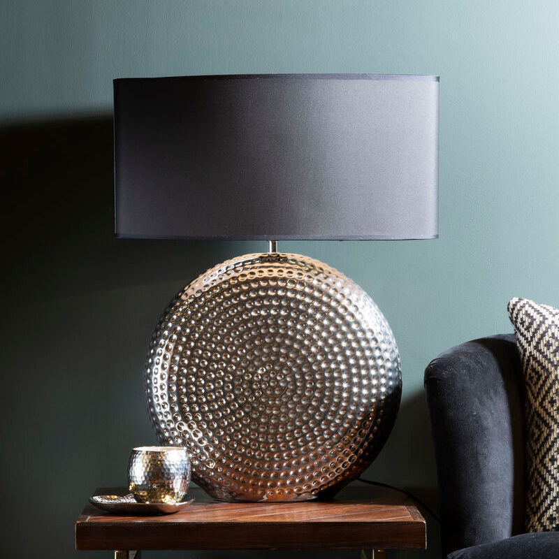 Decorative lamp with textured design on a wooden side table against a dark wall.