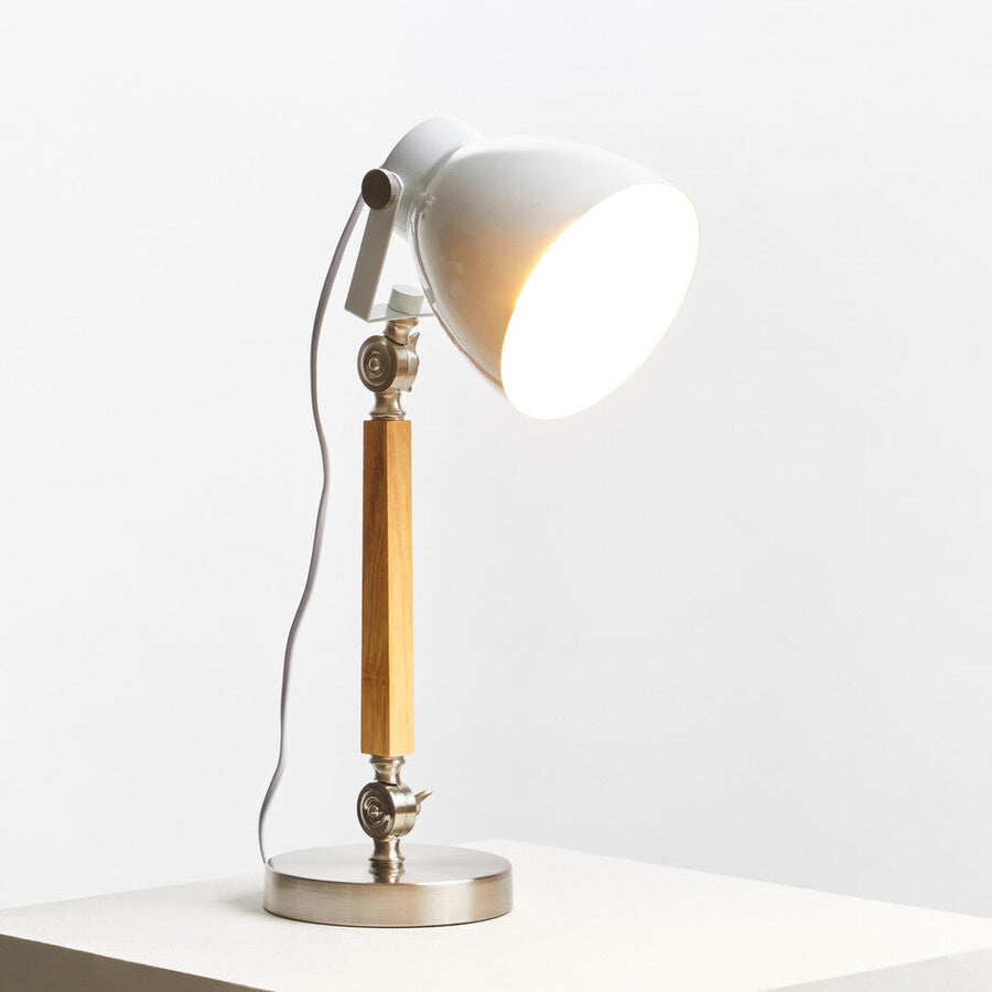 Table lamp with white shade and brass arm on a white surface with light gray background