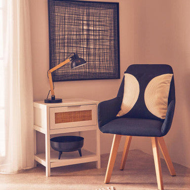 Navy chair with wooden legs in a room with a lamp and framed artwork on the wall.