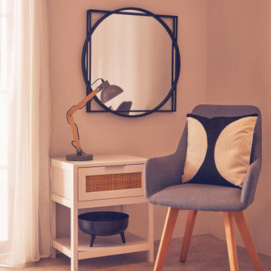 Modern chair with a decorative cushion next to a side table with a lamp and mirror in a room.