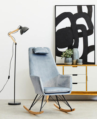 Blue rocking chair in a room with a floor lamp and abstract art on the wall.