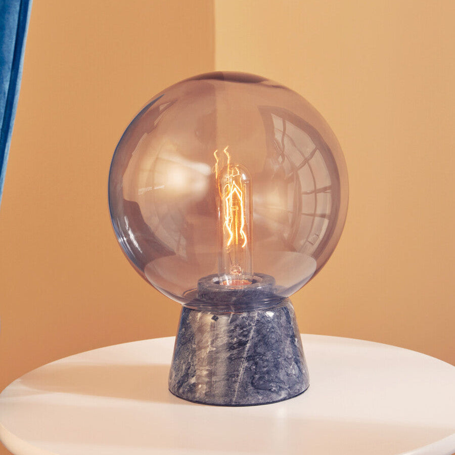 Table lamp with a clear glass shade and marble base on a white surface against a beige background