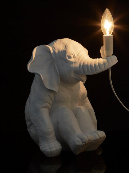 White elephant-shaped lamp holding a light bulb against a black background