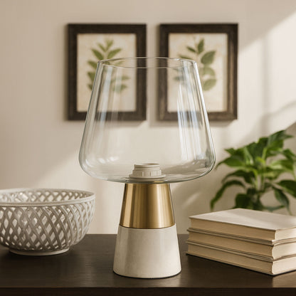Clear glass table lamp with gold and white base on a wooden surface, with books and decorative items in the background.
