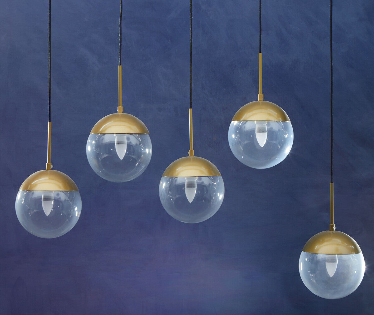 Five pendant lights with gold bases and clear glass globes on a blue background