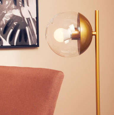 Gold floor lamp with a glass shade next to a red chair against a beige wall.