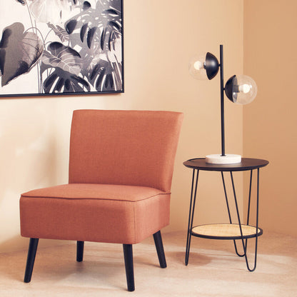 Orange chair and black side table against a beige wall with a leafy artwork.